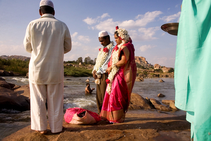 A Muslim couple weds in 2005 alongside the Tungabhadra River at Hampi, south India. In the background, a Hindu man takes his ritual bath. “Muslim Wedding in India”  Claude Renault, 2005, CC-BY-2.0